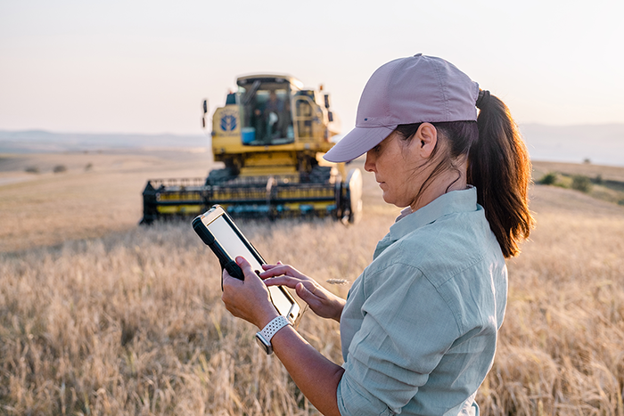 A woman in a field using a tablet to manage farm payroll software.