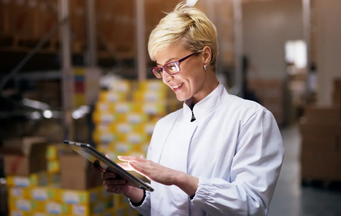 A woman in a lab coat is using a tablet in a warehouse