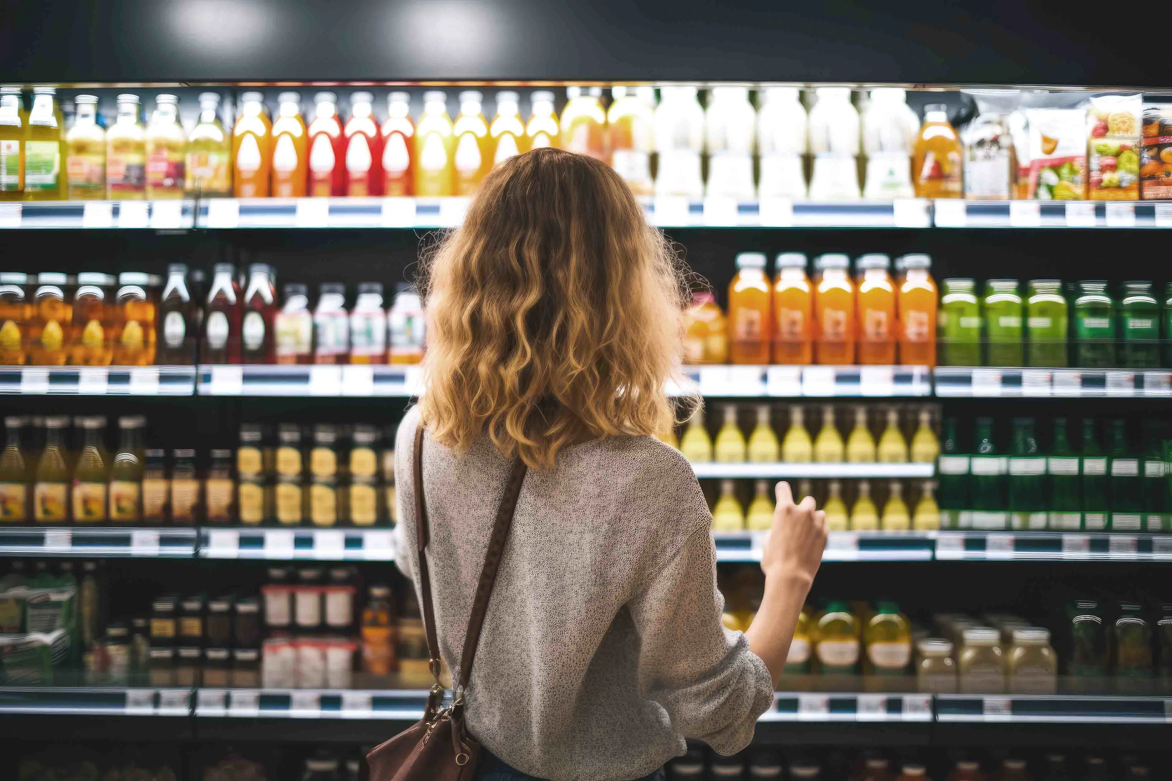 A woman surveys the assortment of beverages in a “perfect store” shelf setup, considering her options for purchase.