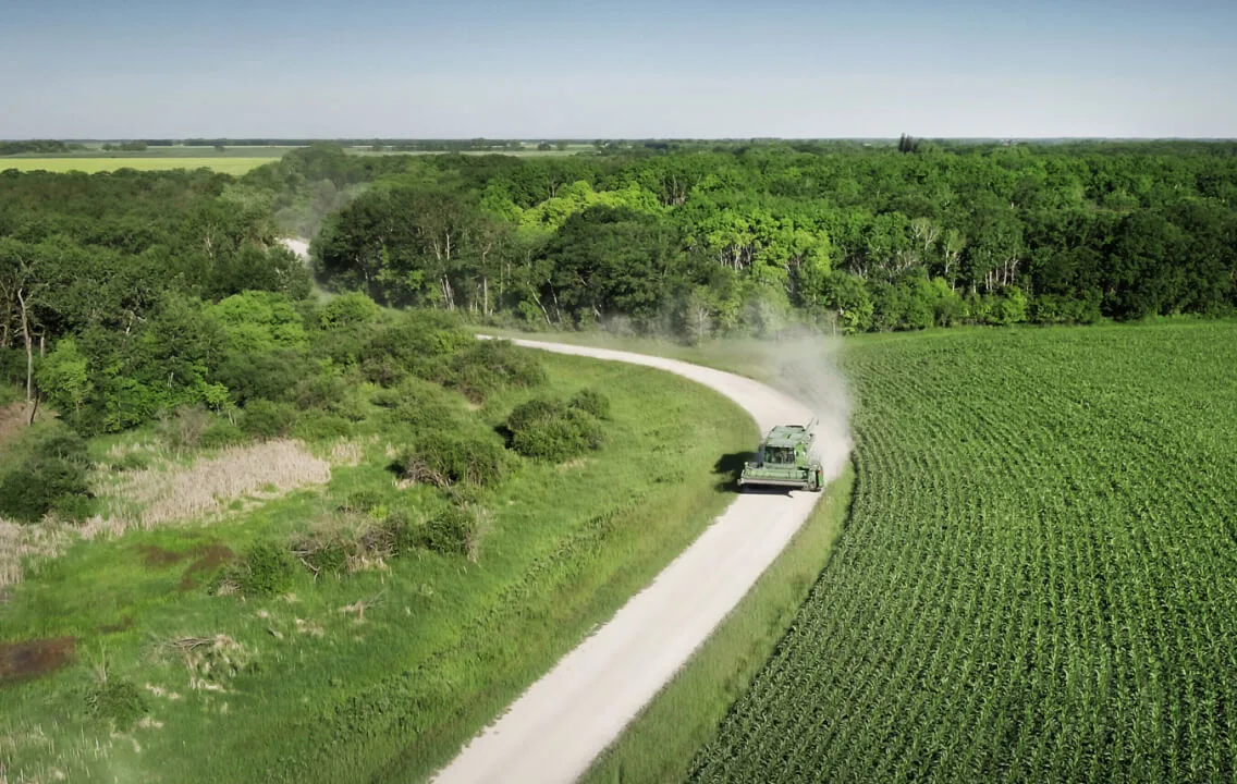 An aerial view of a tractor driving down a road beside a corn field.