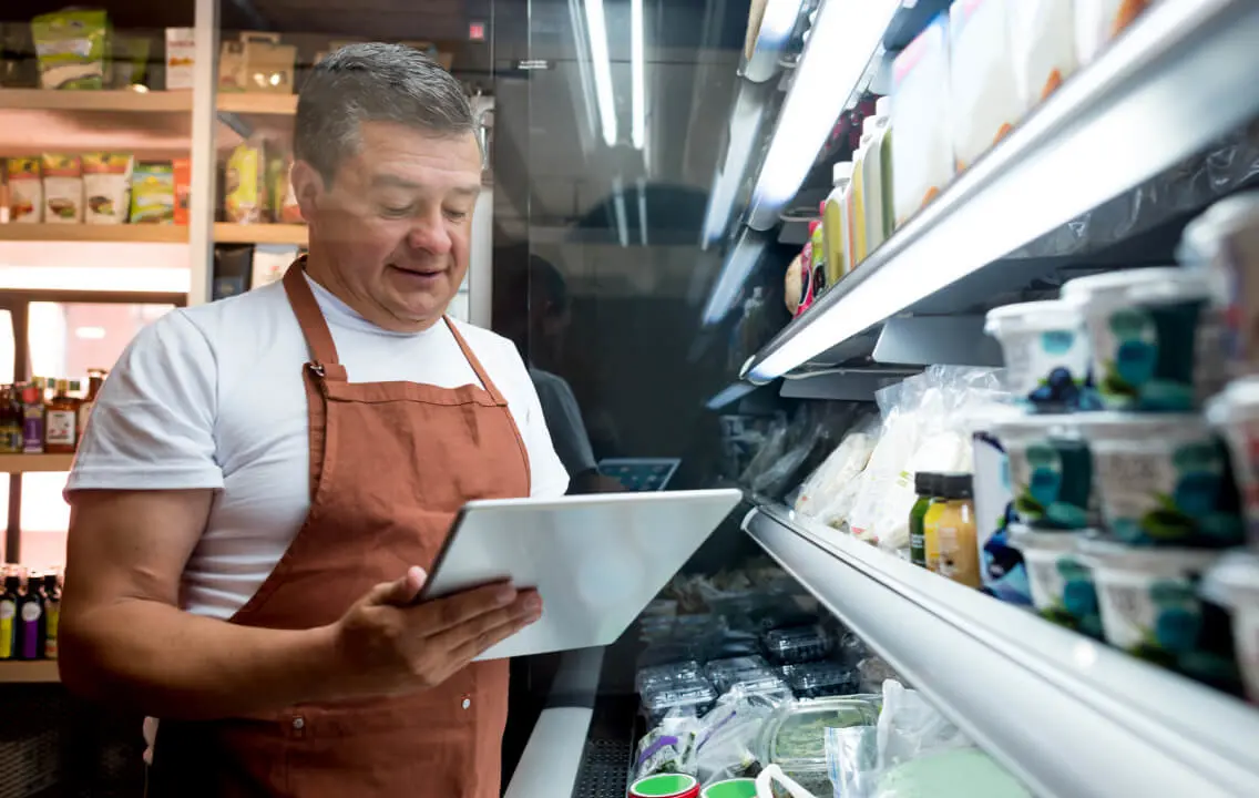 A man in an apron looking at a tablet.