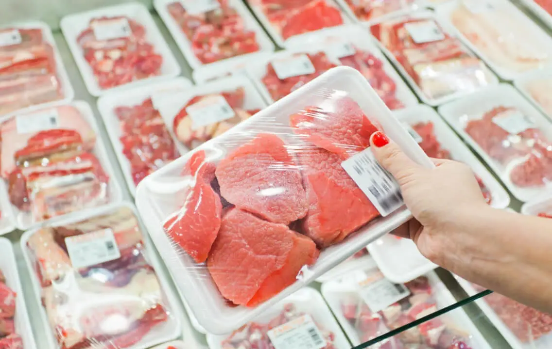 Une femme tient un paquet de viande dans un magasin