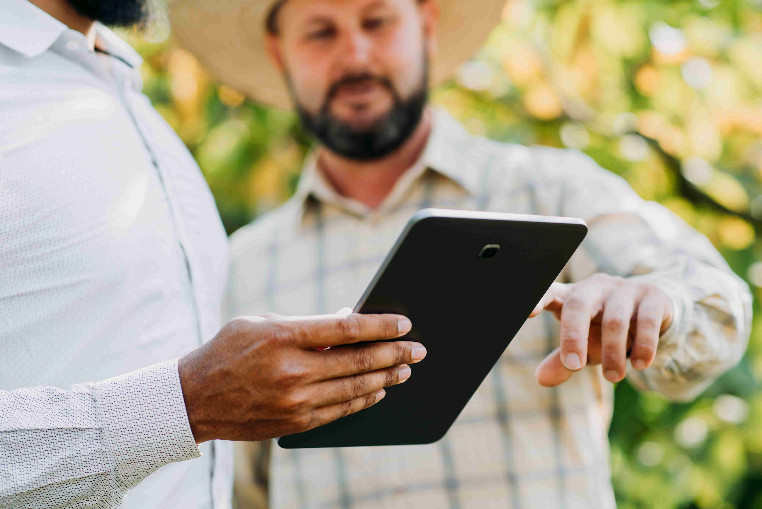 Two men in hats are using a tablet to manage farm accounting tasks.
