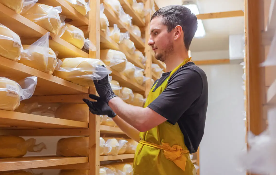 A man in an apron is putting cheese on shelves