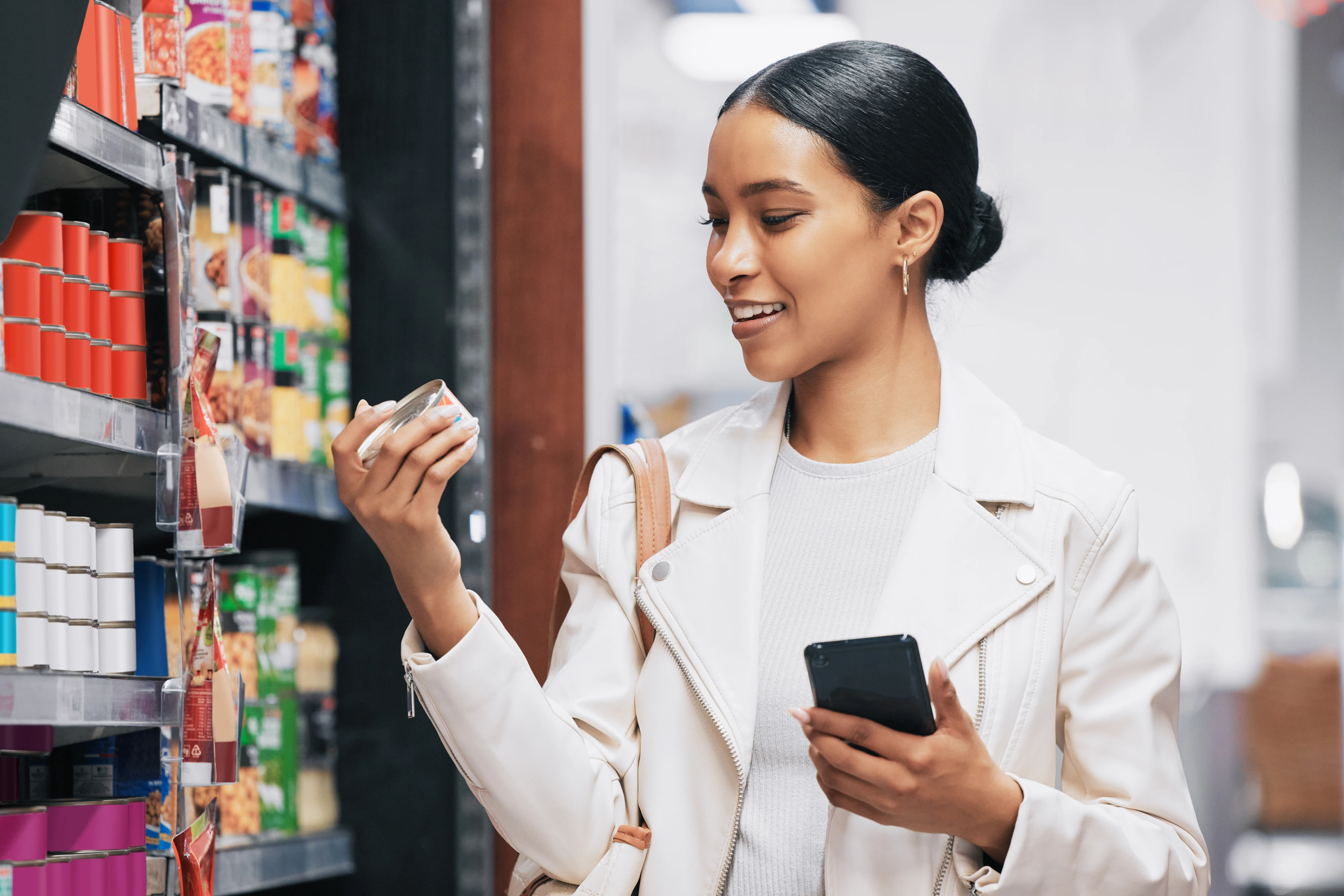 Femme lisant un produit en promotion à l’épicerie avec son téléphone en main.