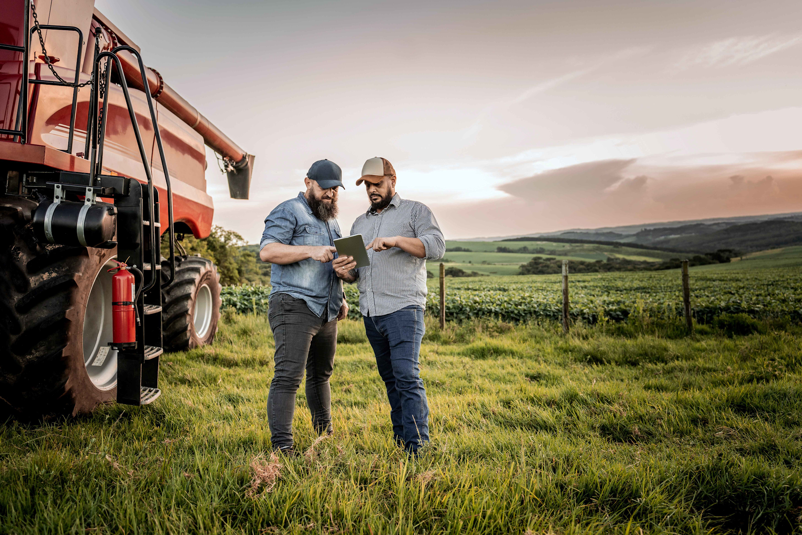 US agronomist & grower with a red tractor in a NA field, using a tablet for real-time crop data.