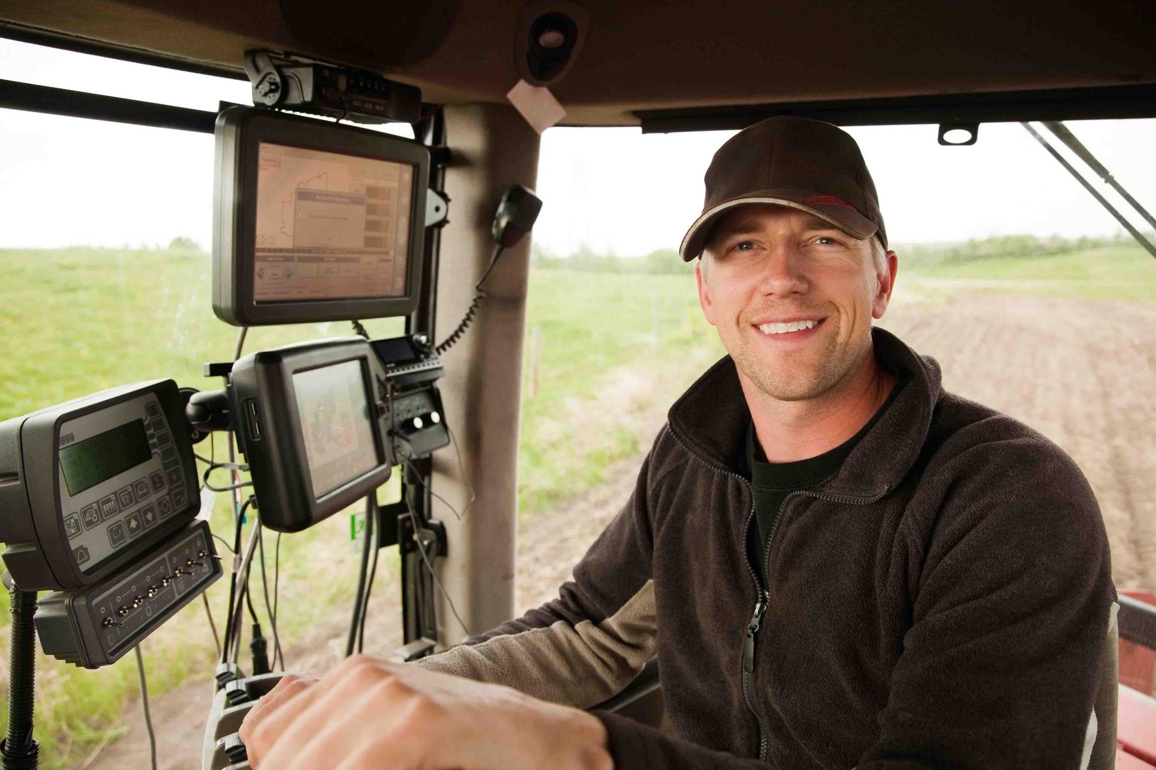 A smiling farmer in a high-tech tractor cab using smart displays for precision agriculture data.