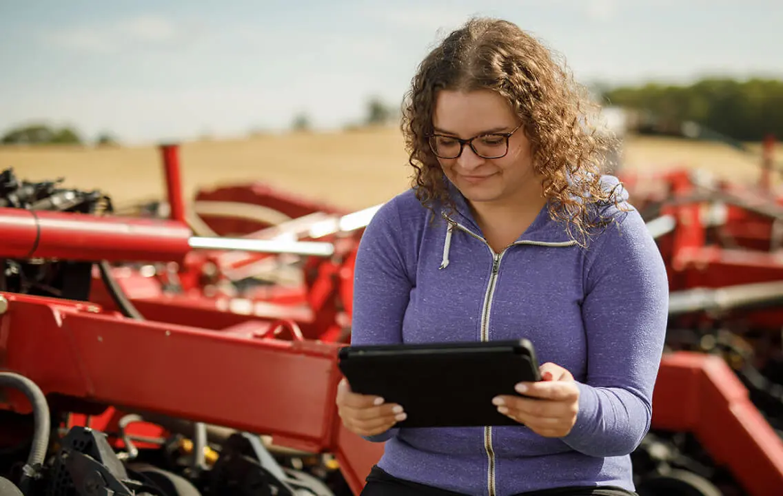 A woman is sitting in front of a tractor, looking at a tablet