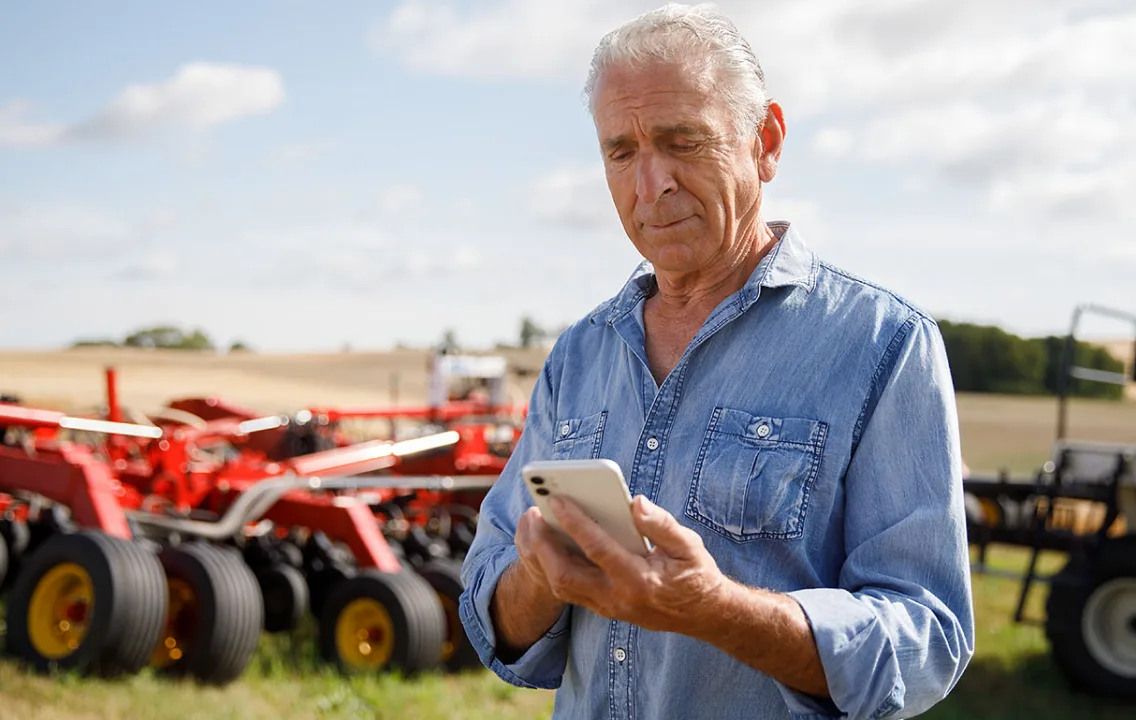 An older man using a cell phone in front of a tractor.