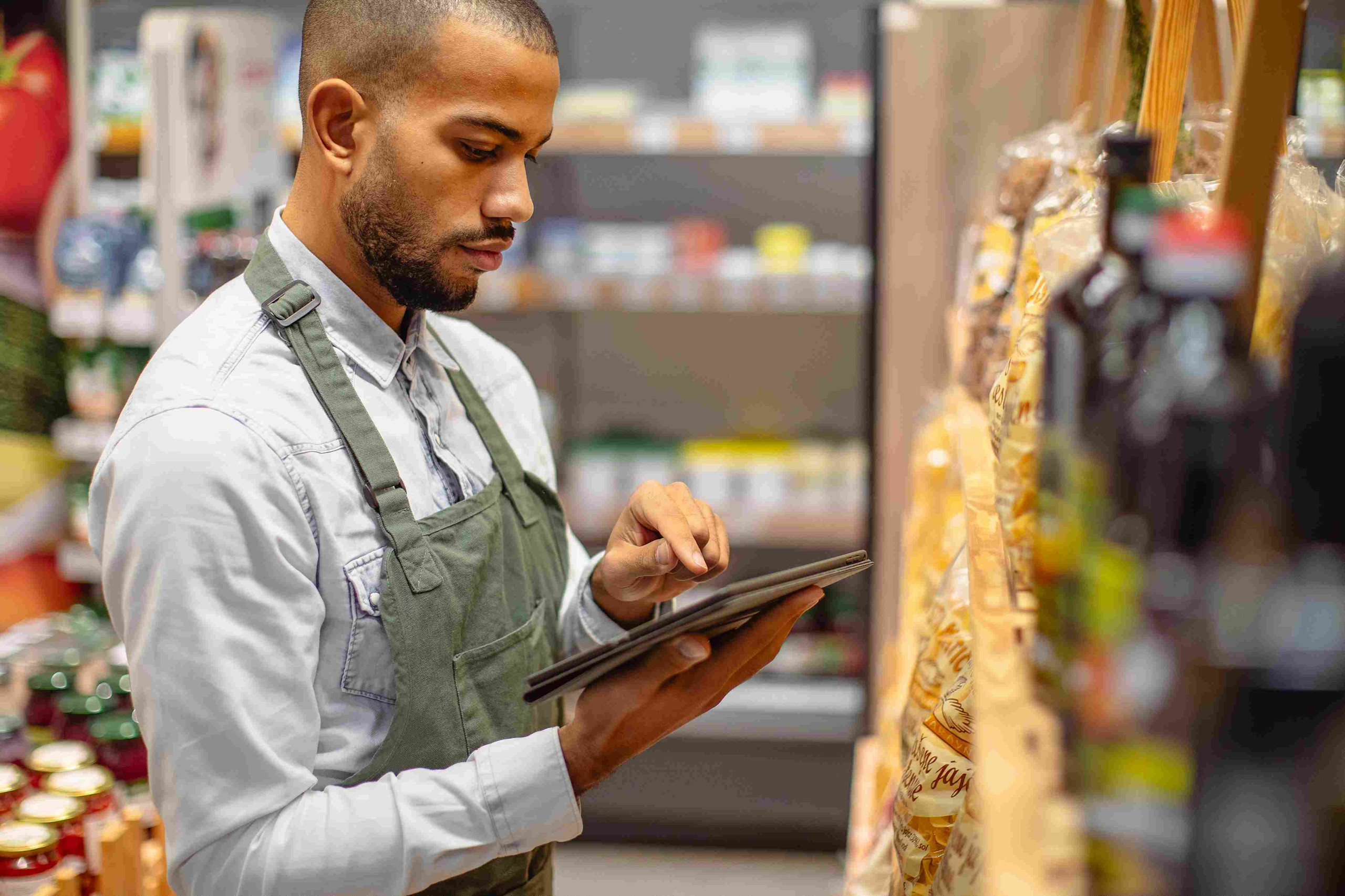 A retail sales representative using a digital tablet to perform a shelf audit in a grocery aisle.

