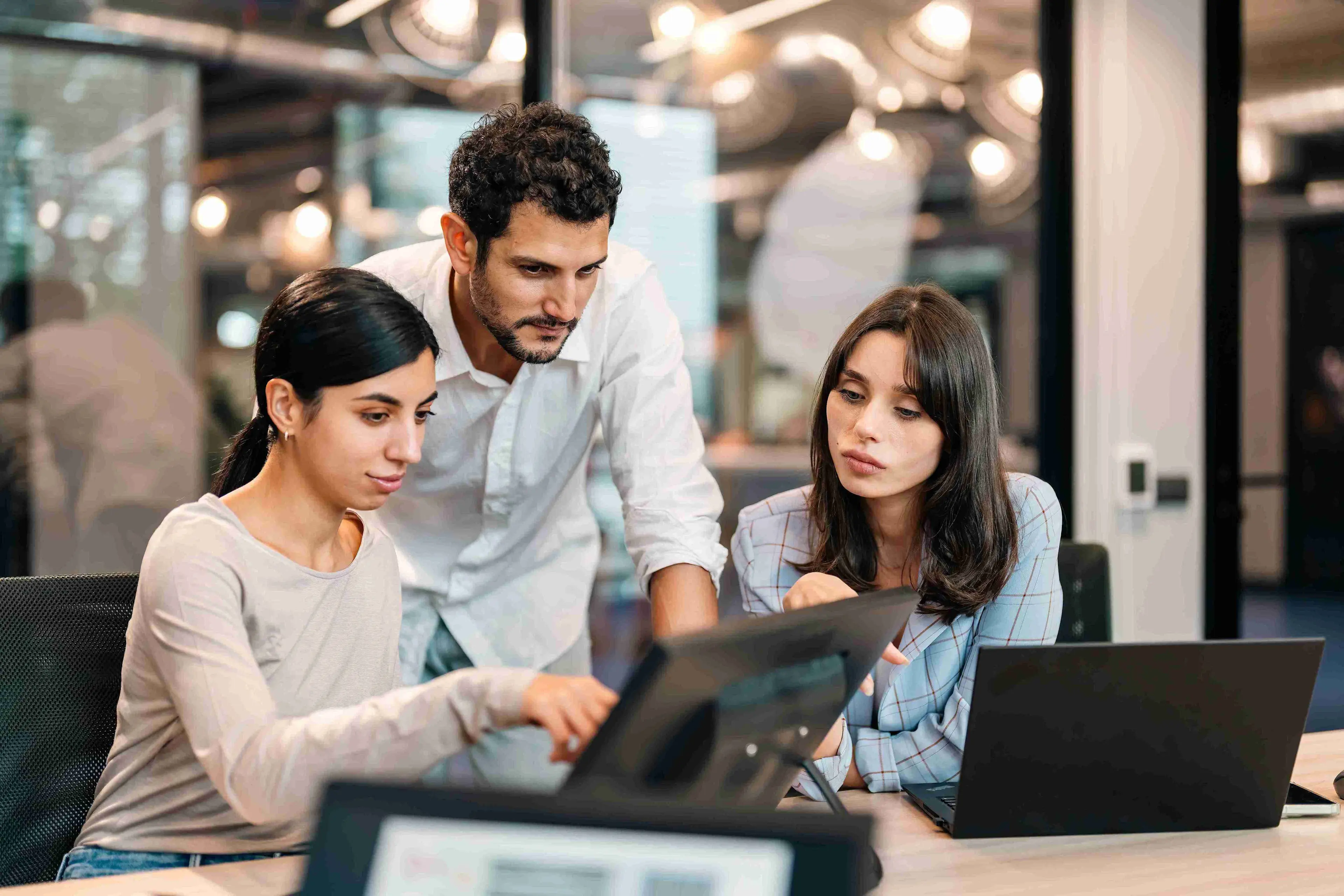 3 colleagues working on laptop, focused on TPM AI strategies.
