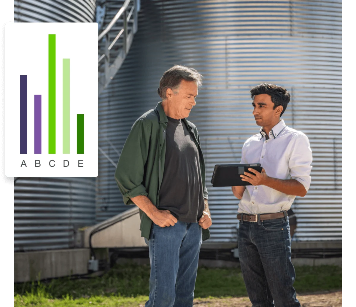 Two men standing in front of a silo, looking at a tablet.