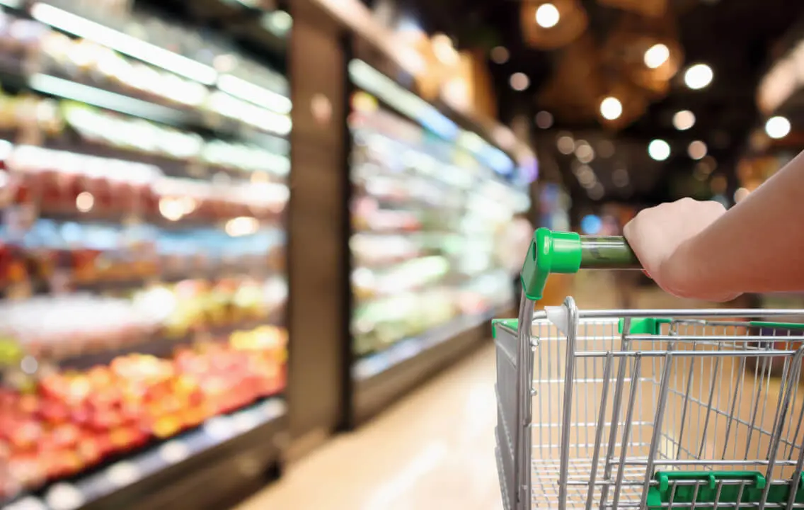 A person is holding a shopping cart in a grocery store.