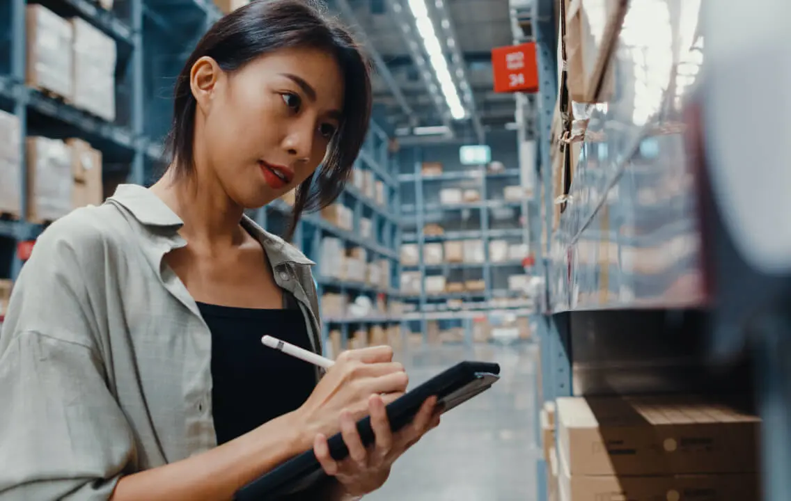 Asian warehouse worker using a tablet in a warehouse.