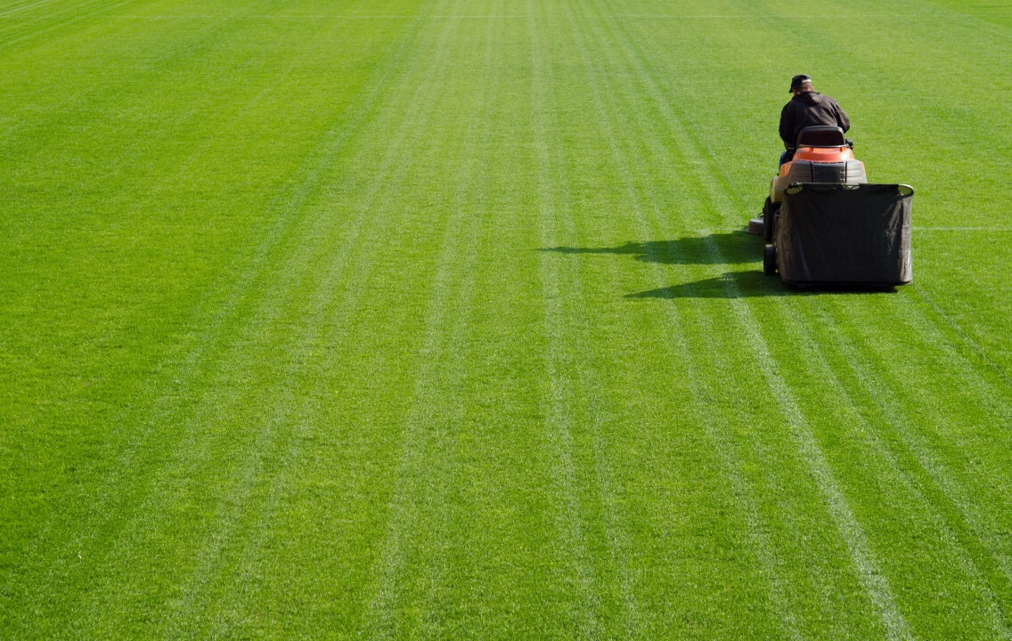 A man is mowing the grass on a soccer field.