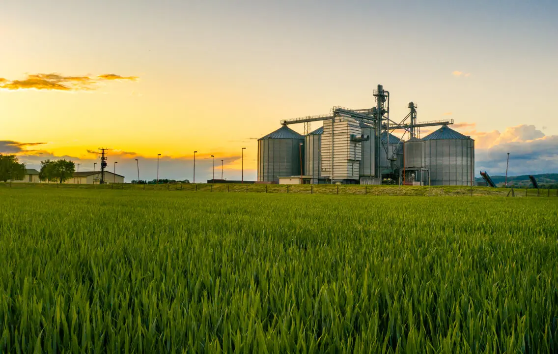 Une ferme avec des silos à grains et un champ vert au  coucher du soleil