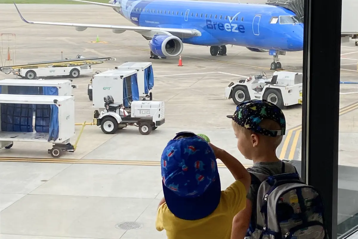 Two children looking out an airport window at a Breeze plane