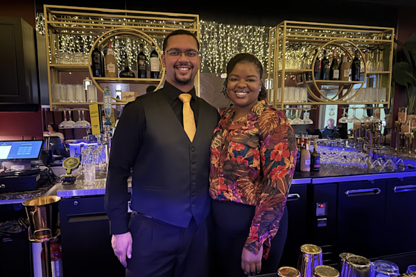 Two people smiling and standing in front of the bar they own