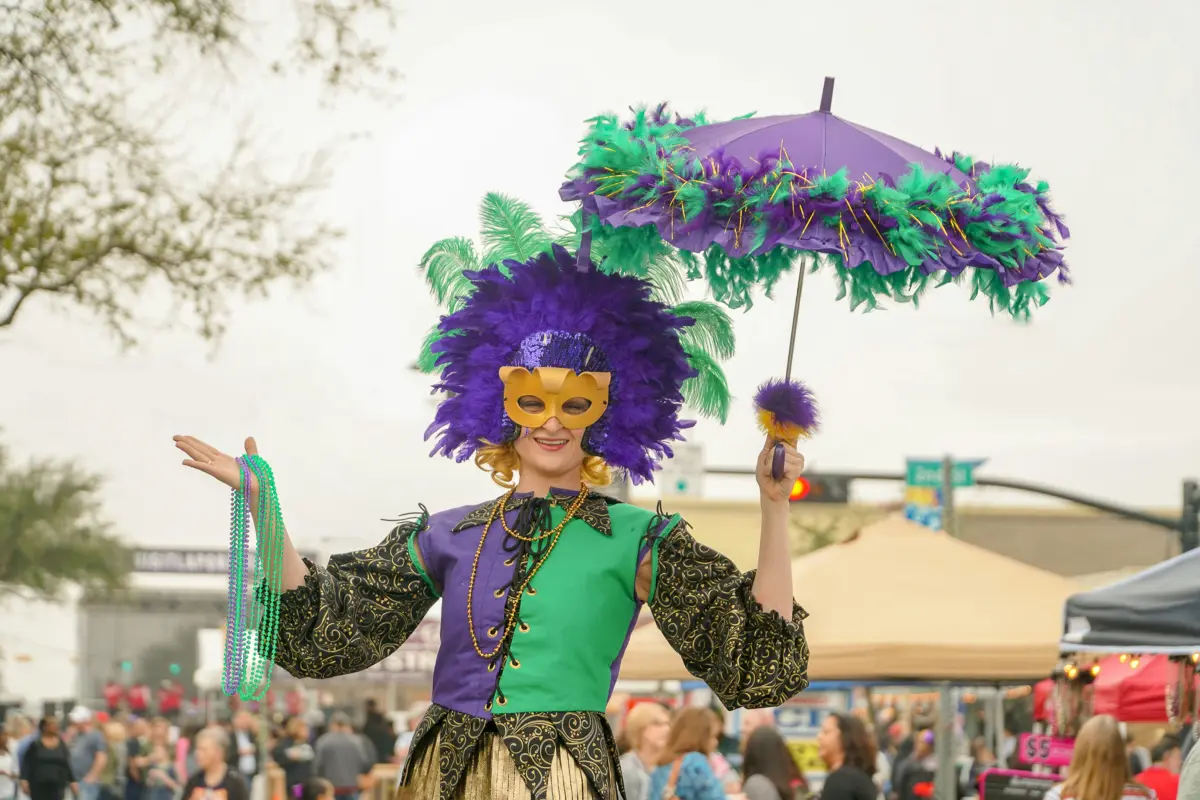 A woman dressed for Mardi Gras holding beads and an umbrella
