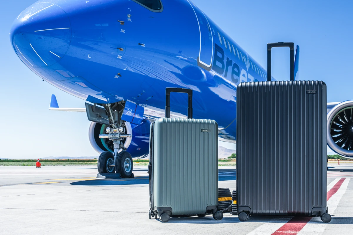 Carry-on and checked suitcases on the tarmac beside a Breeze Airways A220