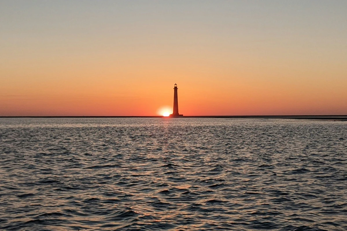 A sunrise over ocean waters with a lighthouse in the distance