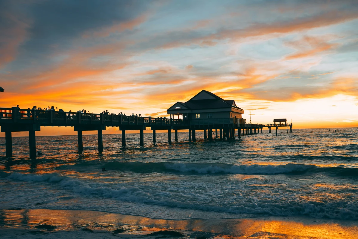 Crowd gathered on the sand watching sunset near a beach pier on the Florida Gulf coast