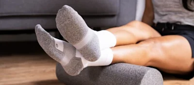 Close-up of grey and white cushioned running socks, feet propped on a foam roller