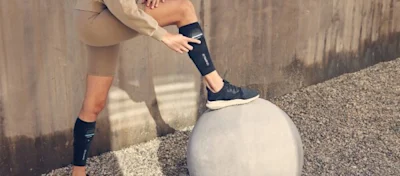 Runner stretching a calf against a concrete sphere, wearing black compression calf sleeves
