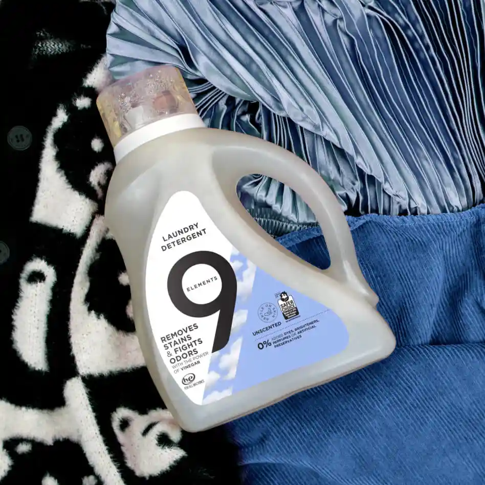 9 Elements unscented laundry detergent bottle laying on the blue clothes and blanket.