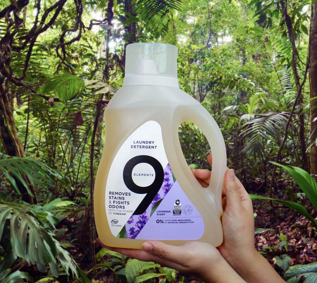 Hands holding Nine elements lavender laundry detergent bottle in the forest.