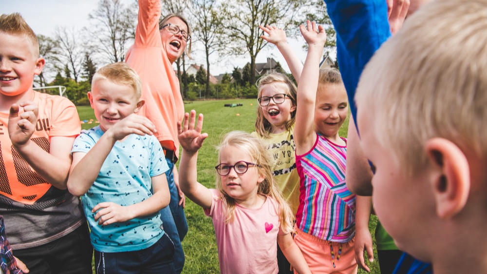 Buiten juichen kinderen op de bso met een pedagogisch medewerker