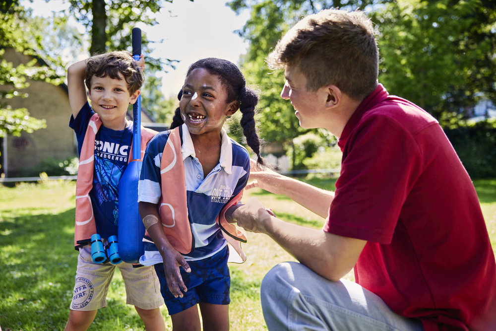 Pedagogisch medewerker met twee kinderen buiten spelen met knotsbal