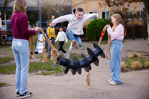 Jongen sprint over zelfgemaakt springtouw, dat meisje en pedagogisch professional vasthouden