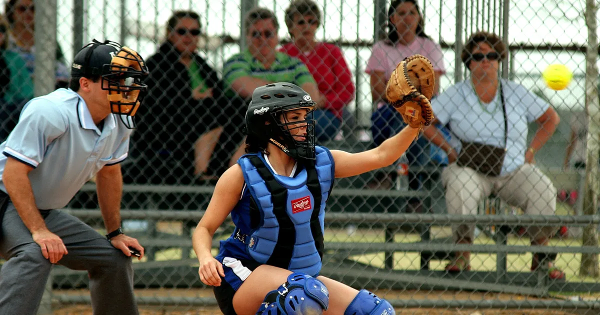 A youth softball catcher during a game with an umpire watching