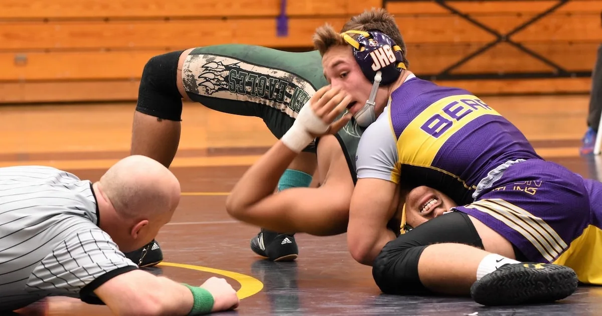 two high school wrestlers and a wrestling referee during a match