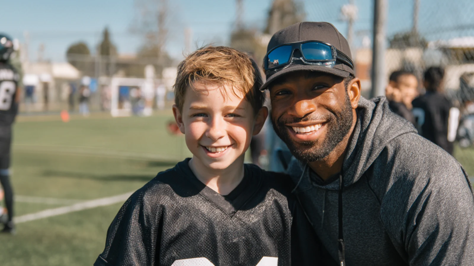 Youth sports volunteer coach with a young football player smiling for a photo