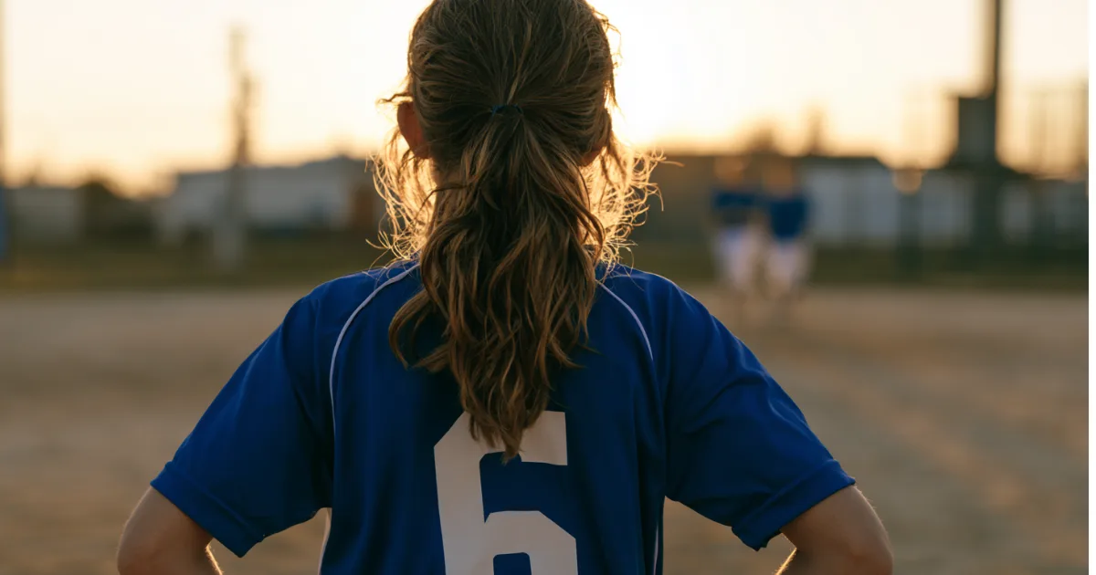 A youth sports soccer player standing with her back to the camera before a game