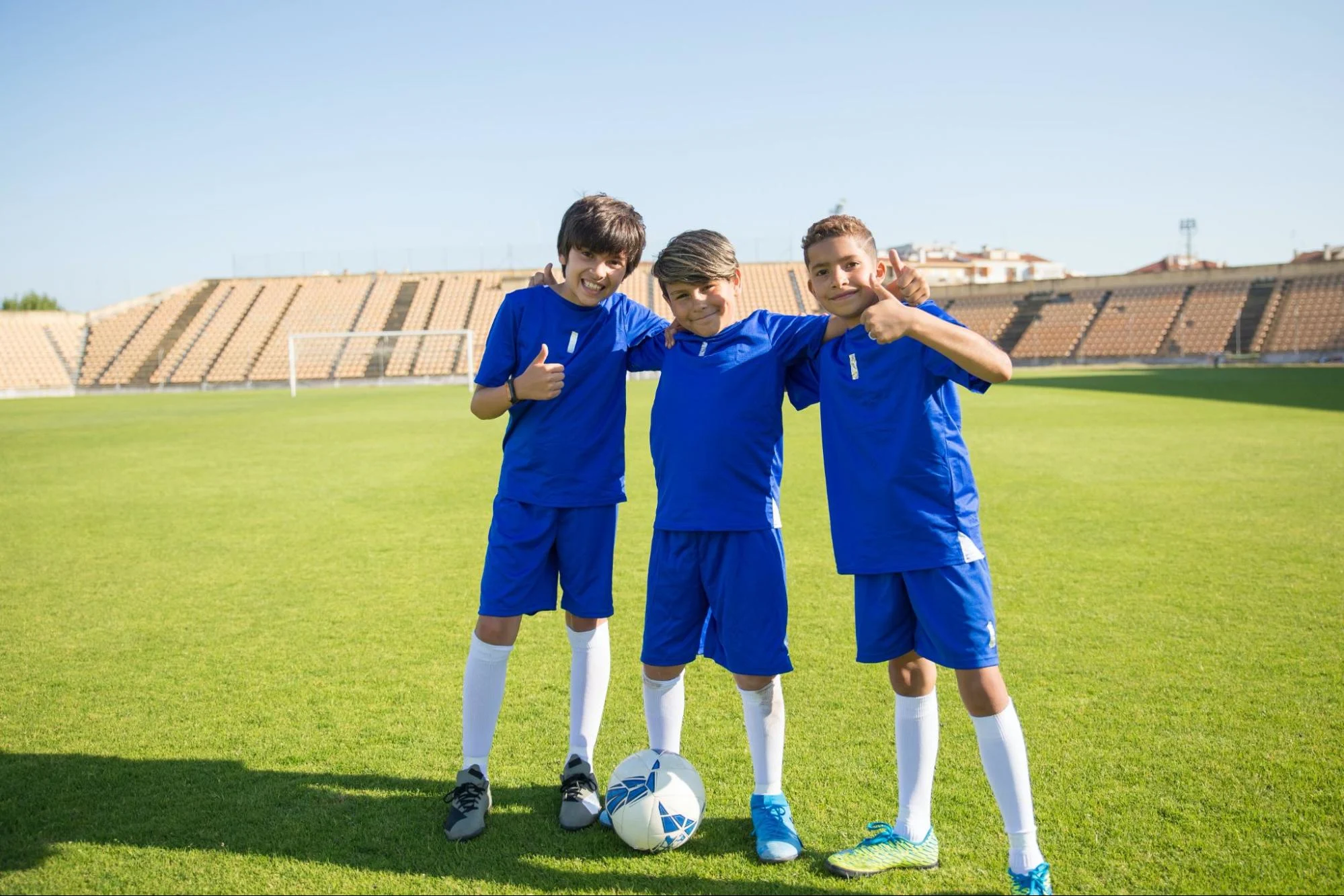 Three youth soccer players giving thumbs up to camera on soccer field