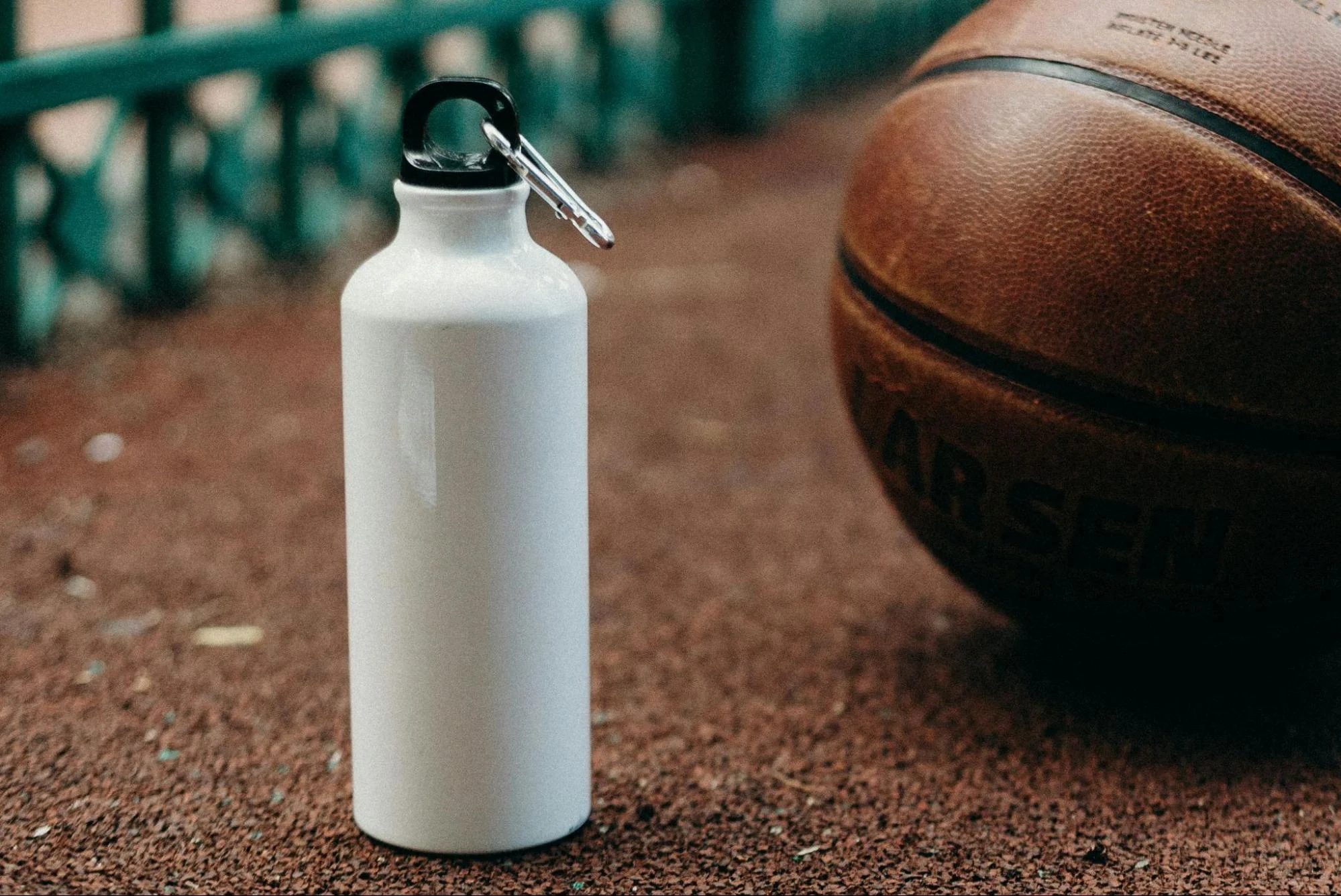 White water bottle and basketball on outdoor court with a green fence in the background