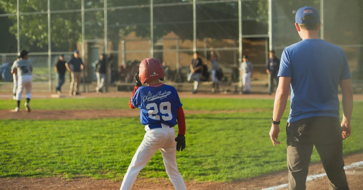 A youth baseball player on base during a game and beside him, is his coach