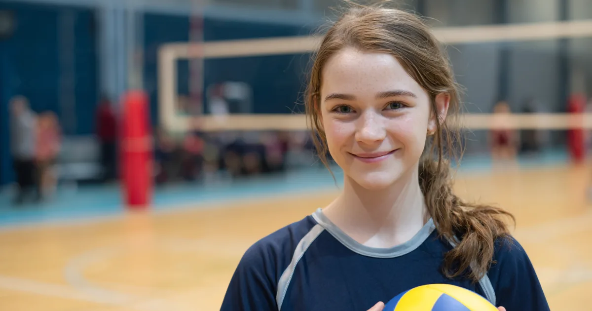 A youth volleyball player holding a ball and smiling at the camera