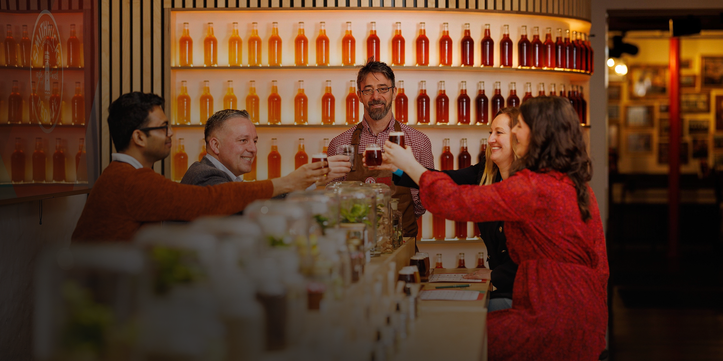 People sitting at a bar, raising glasses for a toast, with shelves of bottles in the background.