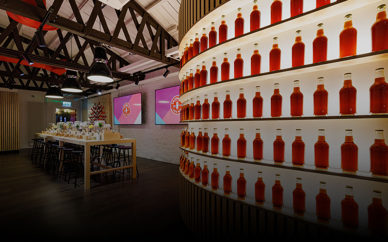 A group takes part in a Smithwick’s tasting experience, with a smiling woman holding a sample bottle while a guide leads the session in a warmly lit room.