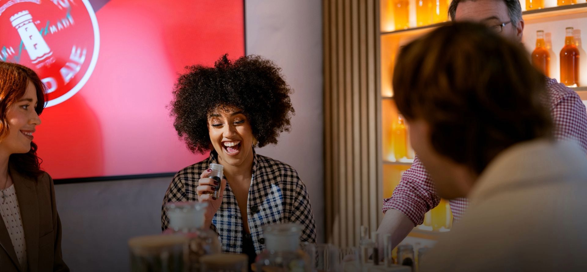 A group takes part in a Smithwick’s tasting experience, with a smiling woman holding a sample bottle while a guide leads the session in a warmly lit room.