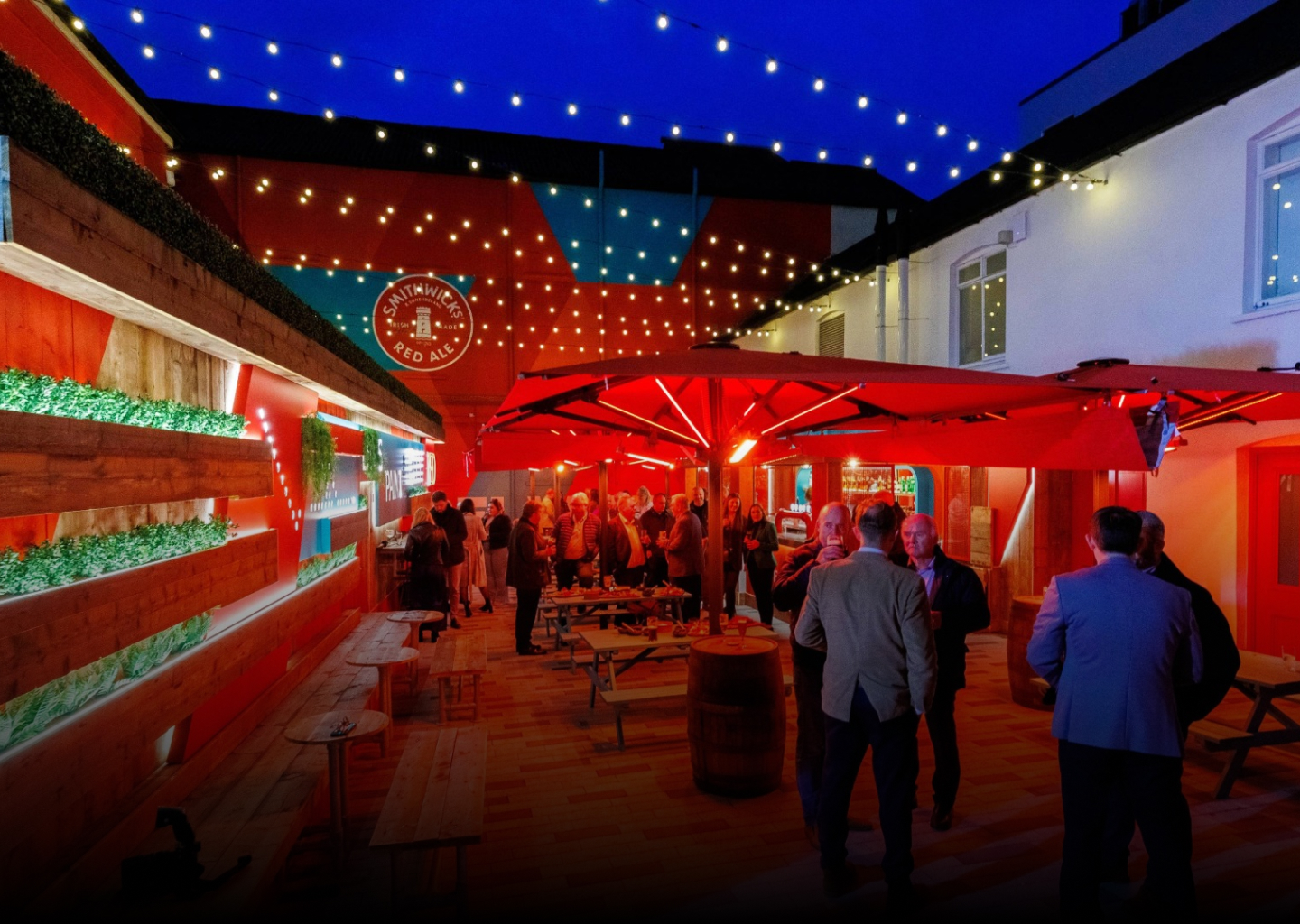 Three friends laugh and raise Smithwick's Irish Ale glasses at an outdoor table at the Smithwick's Experience.