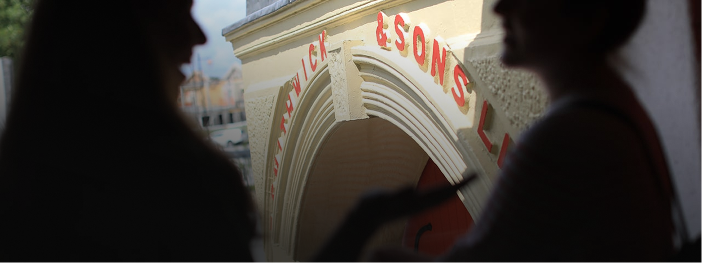 Two people in silhouette talking near a building entrance with red lettering.