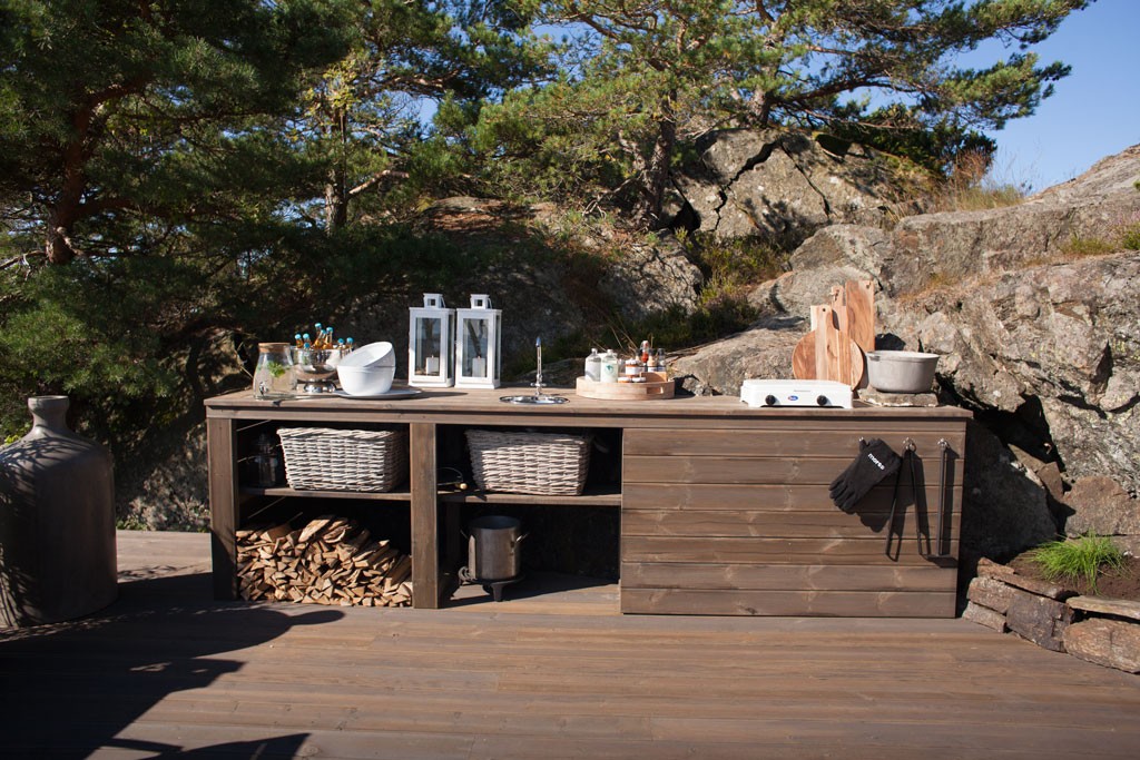 Utendørs brun trekjøkkenøy med ved, kurver, hvite lanterner, skjærefjøler mot berg