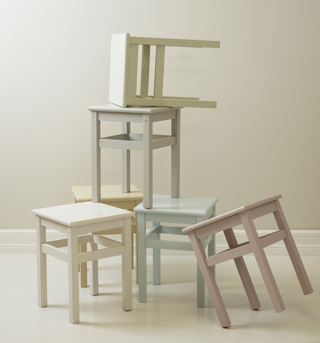 Fem små firkantede krakker i pastellfarger (beige, lys grønn, lyseblå, rosa) stablet ujevnt.