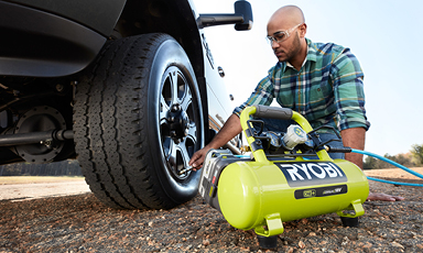 Mann kobler grønn Ryobi-luftkompressor til bilventil ved hjul på grus.