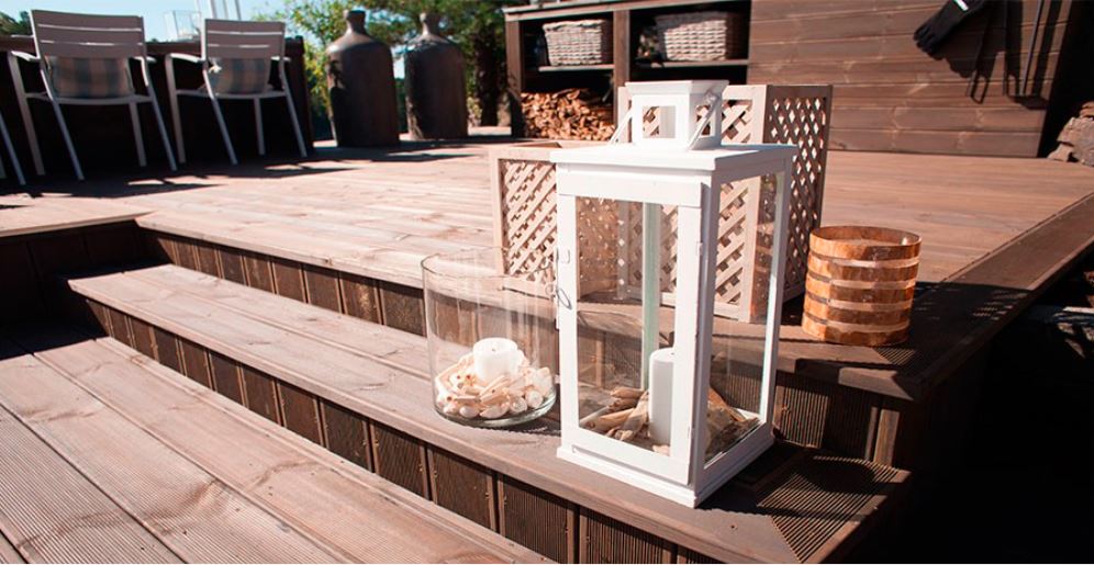 Trelagt dekk med trapp, hvit lykt, glassbolle med skjell, brun kurv og utemøbler